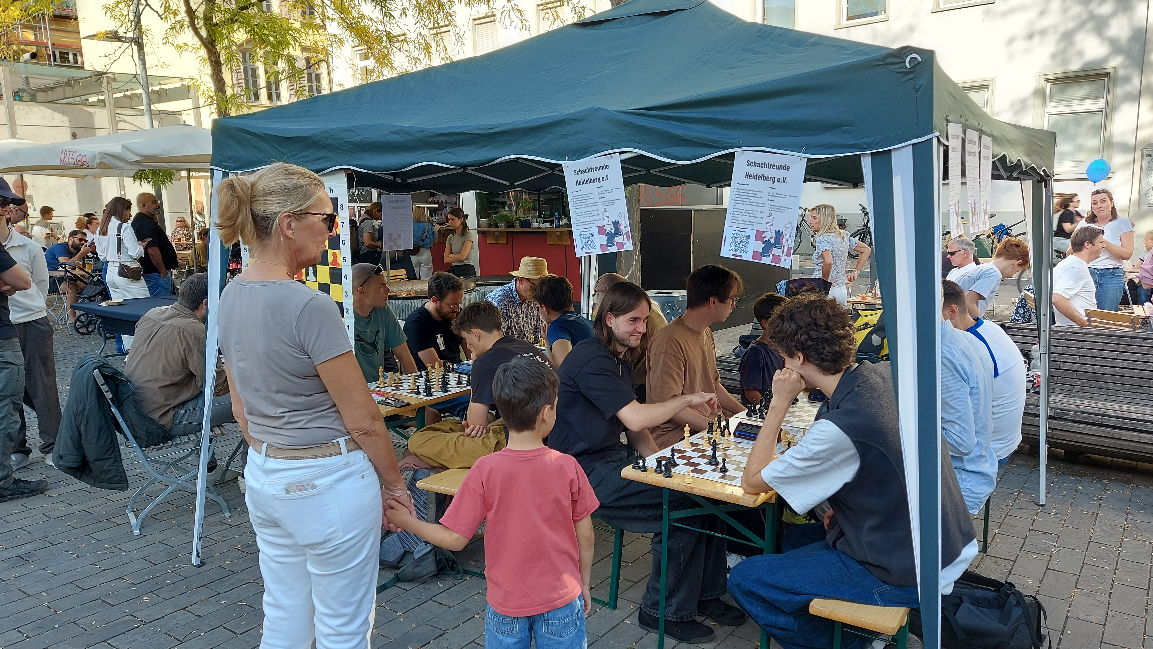 Alle folgenden Bilder ähneln sich und zeigen Erwachsene und Kinder, die in unserem Pavillon an zwei Biertischen Schach spielen. Alle Altersgruppen sind vertreten, von Kindergarten/Grundschulalter bis Senioren.